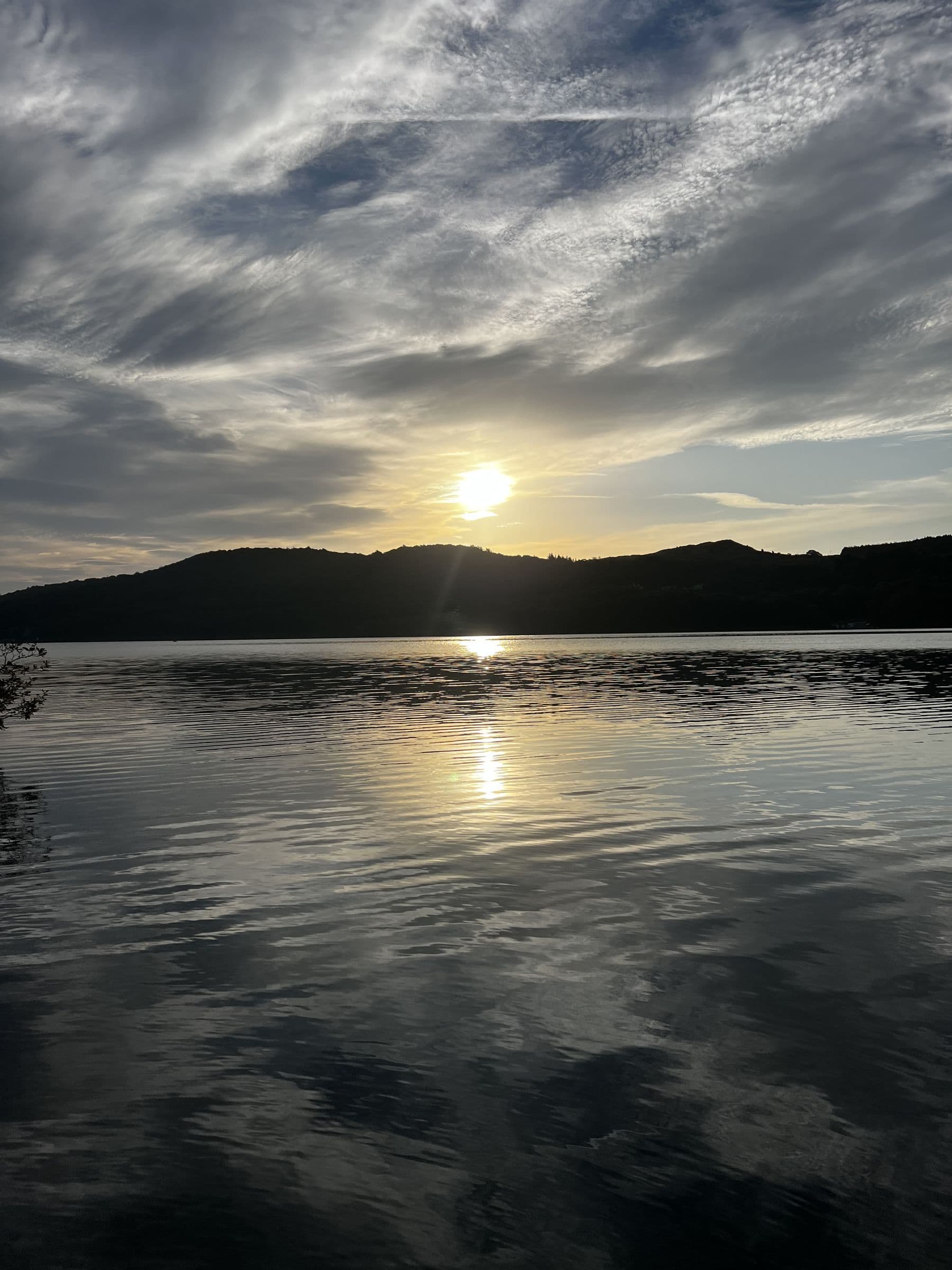 Sunset over the fells across Windermere, the sky streaked with cloud and the sun's path on the water