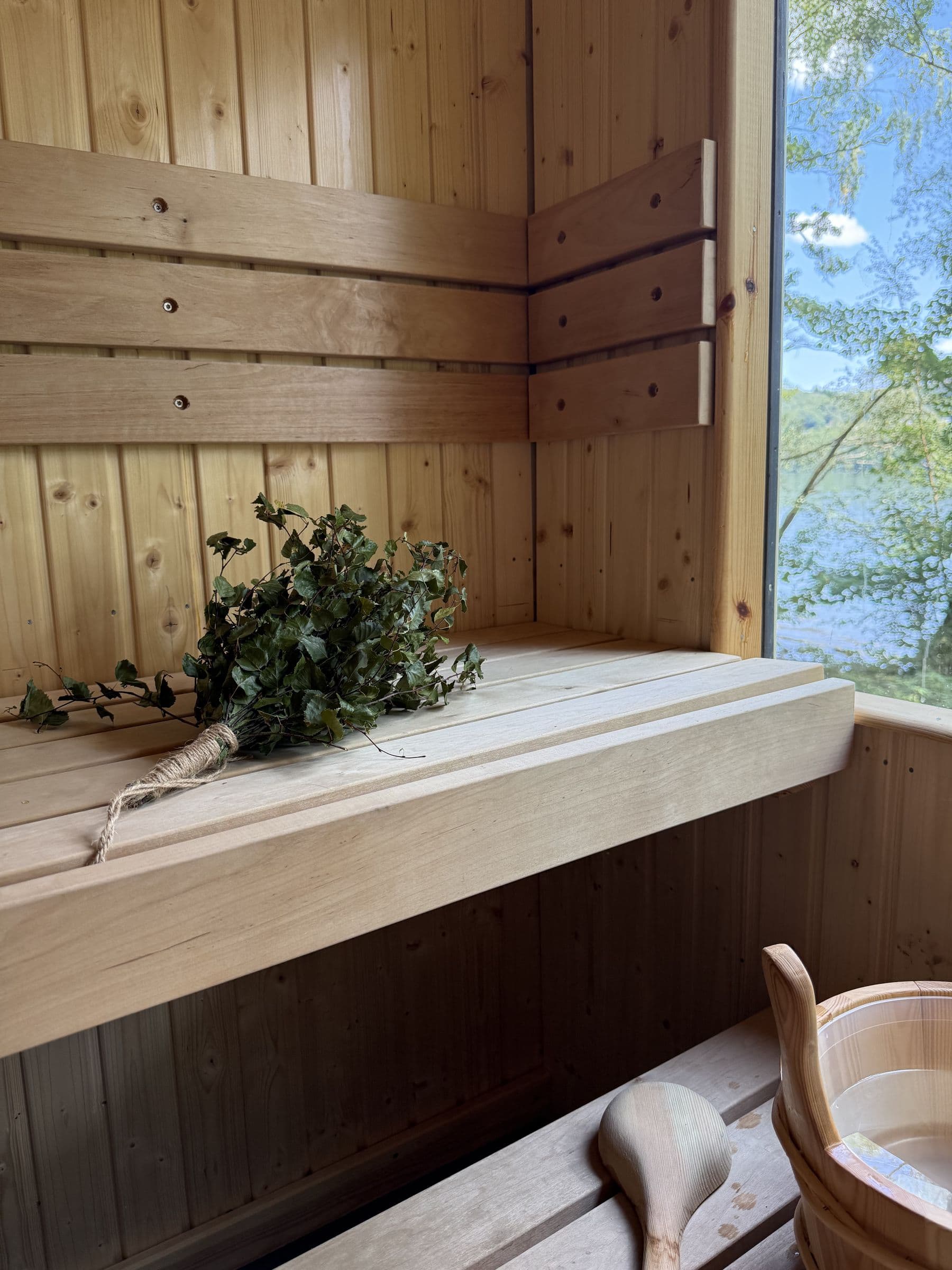 Inside the sauna: a birch whisk tied with twine on the pine bench, with a wooden ladle and bucket on the step below